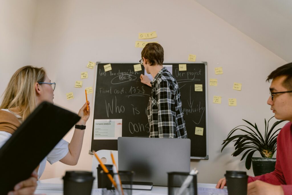 A group of colleagues engaged in a meeting with notes on a blackboard in a modern office.